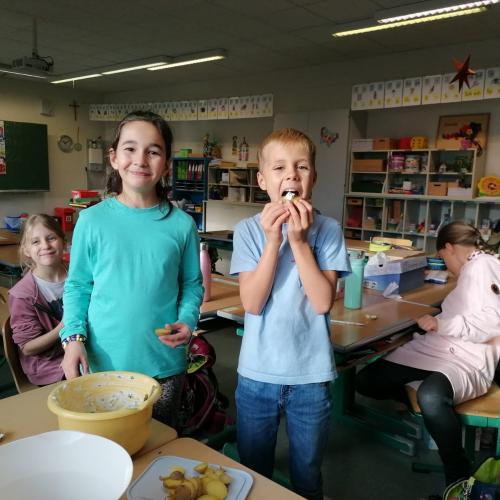 Zwei Kinder blicken in die Kamera. Eines steckt sich genüsslich ein Stück Erdäpfel in den Mund.